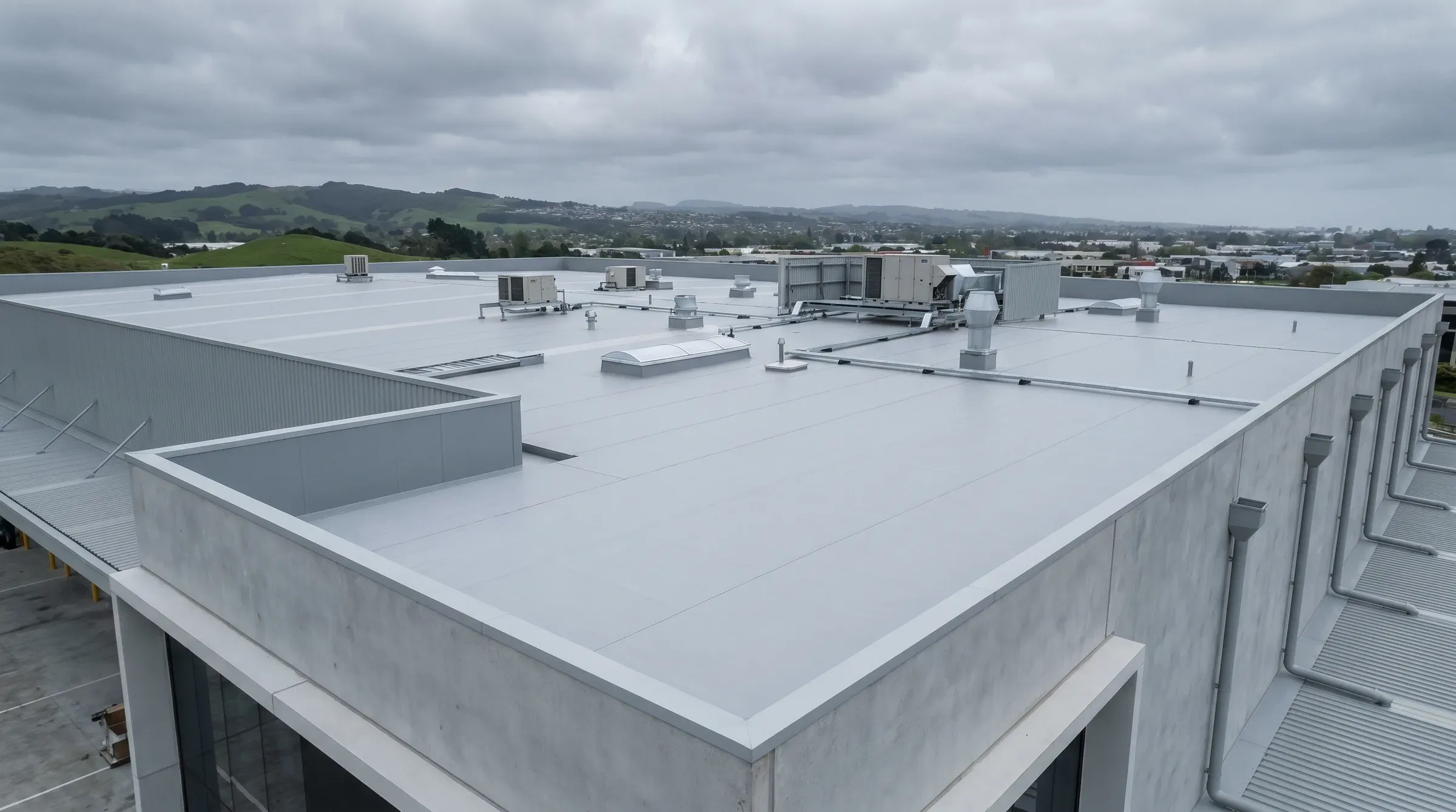Wide-angle view of a completed commercial flat roof on a modern NZ building, with clean geometric parapets and membrane detailing.